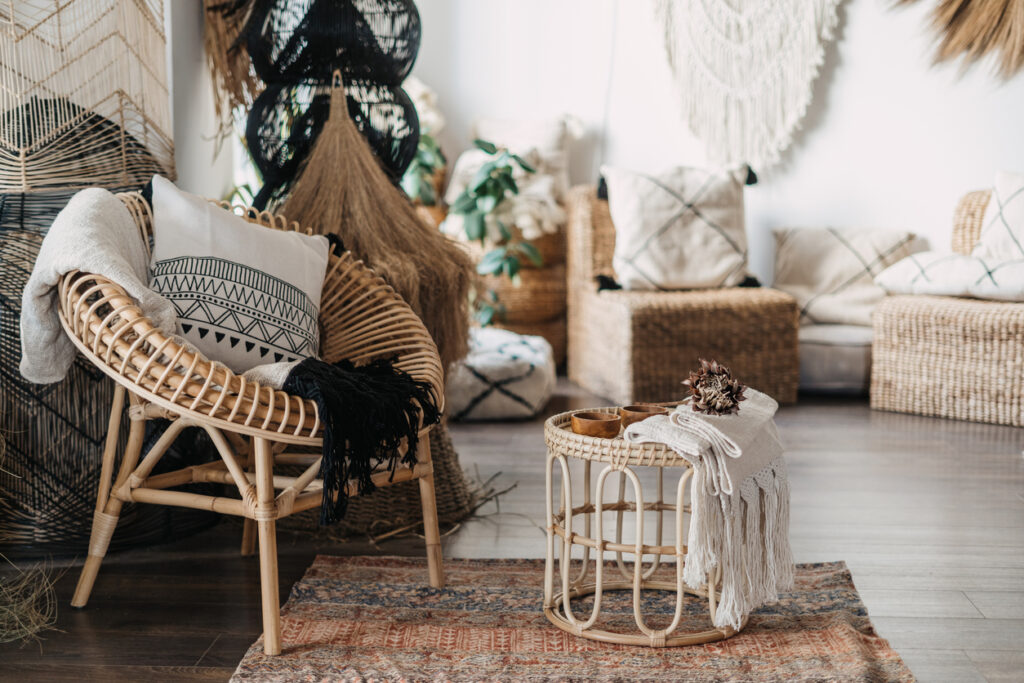 Pohodlná obývacia izba s etnickým interiérovým dizajnom v bohémskom štýle. Byt s domácou výzdobou, ratanový nábytok, kreslo s vankúšmi, bambusový konferenčný stolík, koberec na drevenej podlahe
