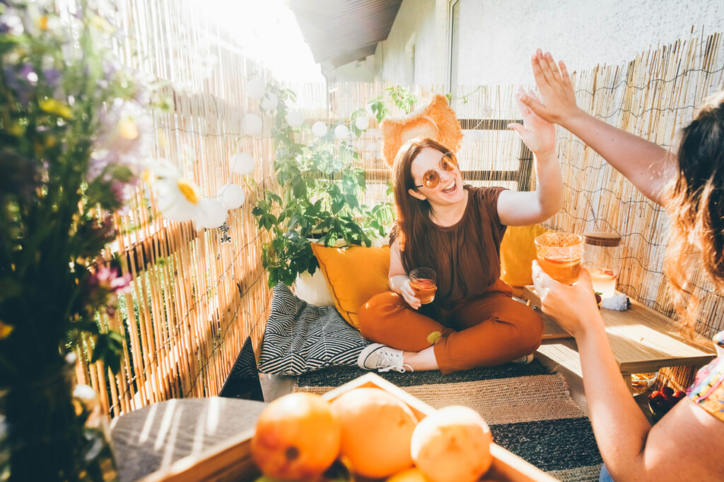 Radostná mladá žena cinká pohármi s lahodnými kokteilmi s priateľkou, s ktorou trávi čas na vyzdobenej terase