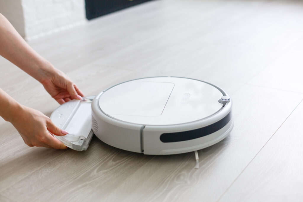 biely robotický vysávač, ženské ruky vkladajú časť na mopovanie 