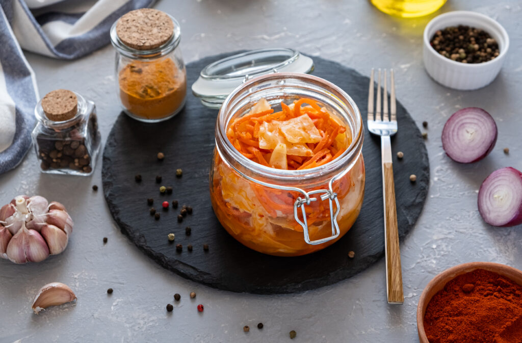 Pikantné kórejské predjedlo kimchi z kapusty s mrkvou v sklenenej nádobe s korením cesnakom a cibuľou na tmavej miske