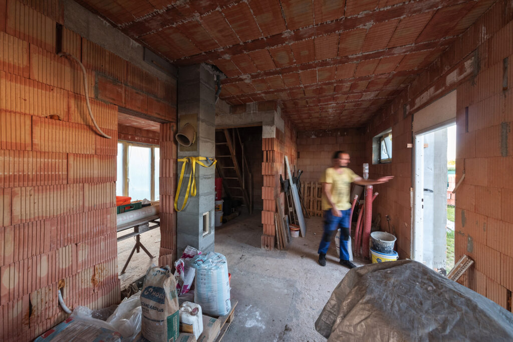 Interiér hrubej stavby domu z tehál HELUZ, pohľad na strop s vložkami MIAKO a stavebný materiál.