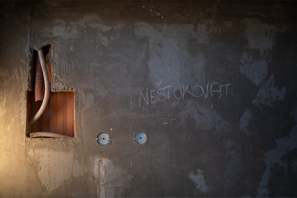 Stena s drážkami pre elektroinštaláciu v murive HELUZ, nápis na omietke v hrubej stavbe.