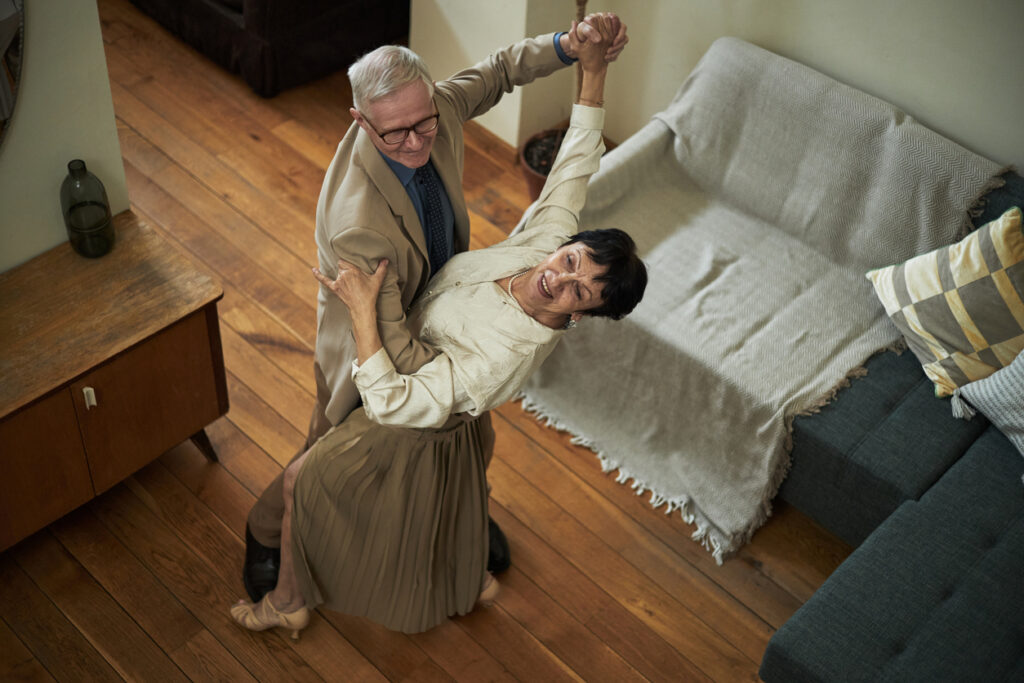 Aktívny seniorský pár tancujúci v obývačke v bezpečne a pohodlne zariadenom interiéri